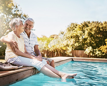 年长的夫妇，在游泳池边拥抱和微笑，在暑假里一起放松、爱或有质量的结合时间。
