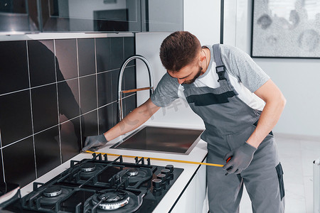 在厨房使用仪表的灰色制服测量台中的年轻专业水管工