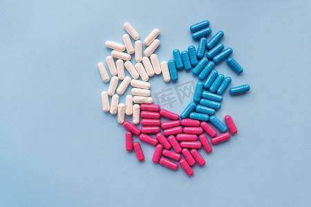 各种颜色的药丸 — 蓝色、粉色、白色，呈心形排列，在蓝色背景中被隔离。