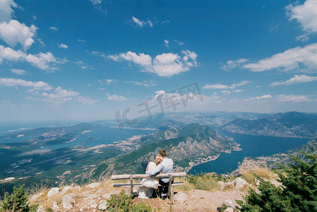 新娘和新郎坐在山上的长凳上拥抱，看着山谷