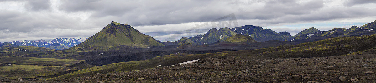 五彩缤纷的全景，冰岛中部自然保护区 Fjallabak 的火山景观全景，绿色的 Maelifell 山和蓝色的积雪山脉，喜怒无常的天空背景