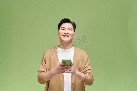 手机绿色背景摄影照片_微笑的年轻人使用被绿色背景隔离的手机