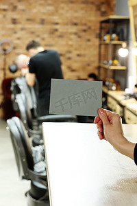 女手拿着灰色明信片或专横的卡片，上面有时尚理发店或美容院背景的模型。