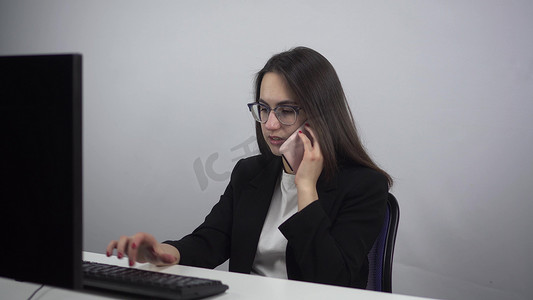 一位年轻的女商人在电脑前工作并打电话。
