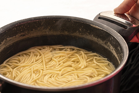 锅里的面条摄影照片_厨师手中平底锅里的意大利面条。