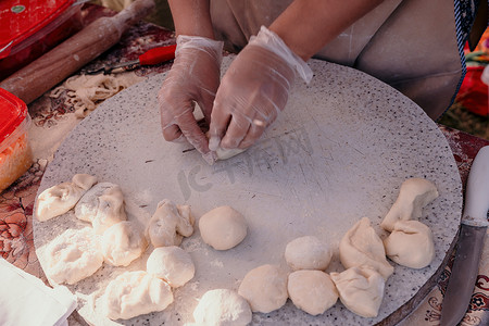美食制作中摄影照片_女人的手用擀面杖和切碎的洋葱在面团中制作 qutab 或 chebureki，用于与阿塞拜疆、鞑靼和希腊美食以及拉丁美洲的肉馅卷饼相关的烹饪概念。