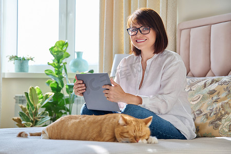 家里的中年妇女坐在沙发上，带着笔记本电脑和猫