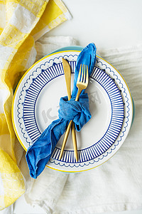 金色餐具系着蓝色餐巾，盘子放在黄绿色亚麻餐巾上。