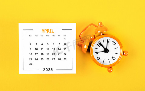 党宣月历摄影照片_2023 年 4 月的 2023 年月历，黄色背景闹钟。