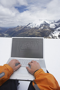 在雪山峰上使用笔记本电脑的人双手特写