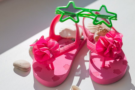 鞋子夏季摄影照片_夏季粉色儿童鞋、儿童拖鞋、婴儿沙滩时装、五颜六色的凉鞋和太阳镜、假日概念。