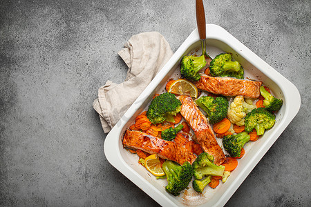 在灰石背景的砂锅菜中，可以看到健康的烤鱼鲑鱼排、西兰花、花椰菜、胡萝卜。