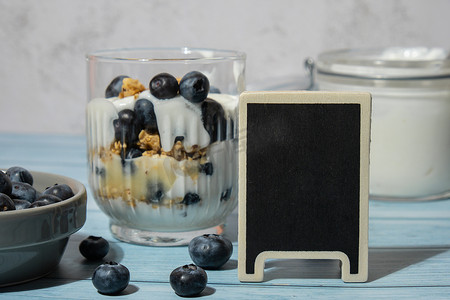 早上格兰诺拉麦片早餐配自制希腊酸奶，蓝色木制背景眼镜中的蓝莓。