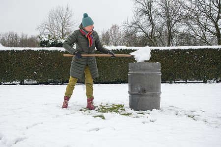 雨循环摄影照片_中年妇女正在用铲子在桶里收集雪，自然资源
