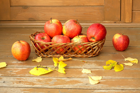 秋天的静物生活，柳条篮里放着成熟的红苹果，木面上散落着黄叶，特写