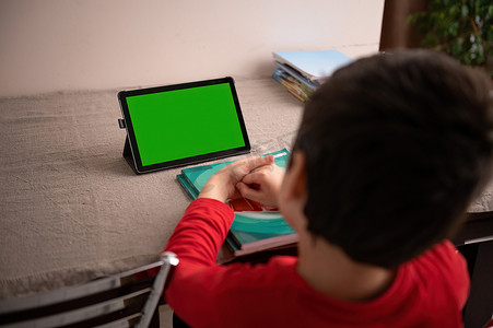聪明的学生坐在桌子上，在带有空白绿色色度键屏幕复制空间的数字平板电脑上观看在线课程