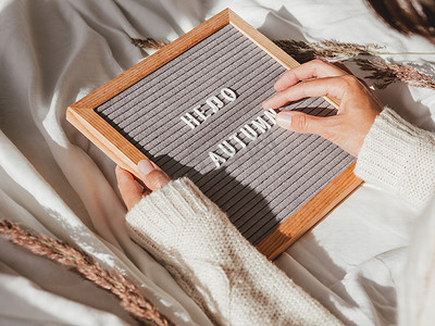autumn字母摄影照片_穿白色针织毛衣的女人在字母 boa 上打字 HELLO AUTUMN