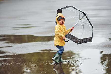 雨后穿着黄色防水斗篷、靴子和雨伞在户外玩耍的孩子
