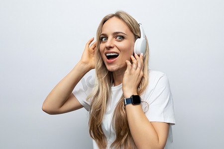 戴着白色耳机的情绪化年轻女性在白色工作室背景下收听播客