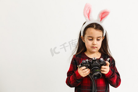 复活节快乐的概念：一个可爱的小女孩，长着粉红色的兔耳朵或拿着相机的兔耳朵