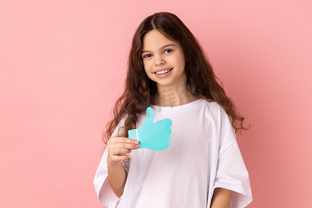 微笑高兴可爱的小女孩拿着并展示喜欢或竖起大拇指的纸形标志。