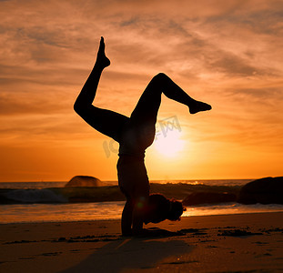 手倒立摄影照片_在晚间锻炼或放松运动训练中，在日落海滩、海洋或海上进行瑜伽、侧影或倒立。