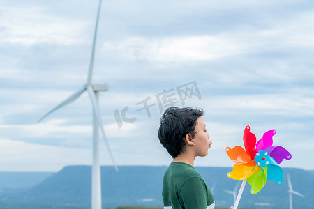 进步的年轻亚洲男孩在风力涡轮机农场玩风车玩具。