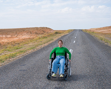 坐在轮椅上的女人在草原的高速公路上。