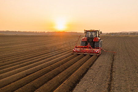粮食危机摄影照片_日落时在农田工作以避免粮食危机的红色拖拉机