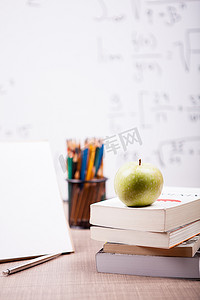 笔记本旁边的一堆书上的青苹果和 t 上的铅笔