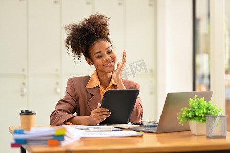 满意的非洲裔美国女员工看着平板电脑，在她的办公桌上查看在线信息