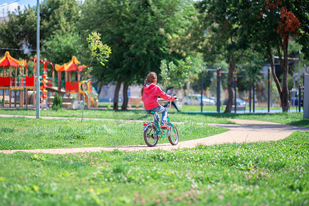 儿童自行车摄影照片_女孩在夏日公园骑儿童自行车