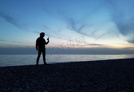 一个人在美丽的夕阳下以大海和云彩为背景的剪影在他手中是无人机的遥控器