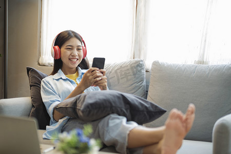 年轻的亚洲女人微笑着在家里使用智能手机听音乐。