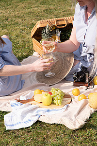 两个穿着夏日长裙的年轻女人正在野餐，草地上的毯子上休息