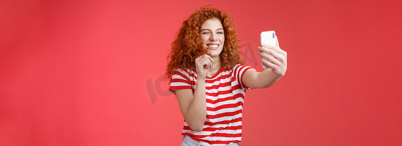 时髦漂亮时尚魅力红发女性卷发发型眨眼厚颜无耻的表情使调情变态的脸拿着智能手机自拍记录视频消息播放有趣的面部过滤器
