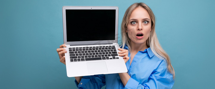 一张震惊的可爱金发女孩的照片，她带着开放式笔记本电脑，蓝色背景上的网站有空白空间