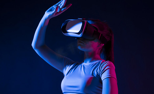 界面交互摄影照片_戴着 VR 耳机并与虚拟现实界面交互的女性。
