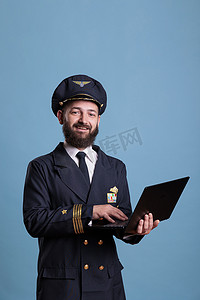 微笑的班机飞行员使用笔记本电脑，键入消息侧视图