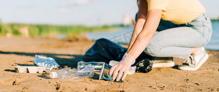 捡摄影照片_年轻的女志愿者手满意地捡起垃圾、塑料瓶和咖啡杯，用大海清理海滩。