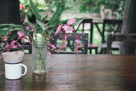 装饰在桌子上的玻璃瓶中的粉红色花朵和绿叶