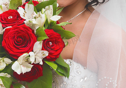 新娘身穿白色婚纱，头戴面纱，手里捧着一束美丽的白玫瑰和红玫瑰，特写