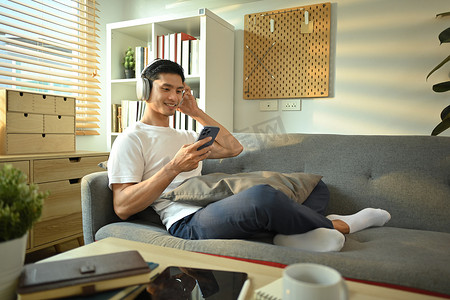 放松的千禧一代人在家里用耳机听音乐、播客或有声读物，在沙发上使用手机