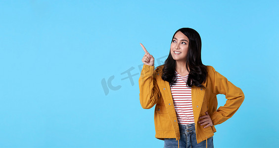 广告浅蓝色摄影照片_微笑快乐的亚洲女人用她的手指指向孤立在浅蓝色横幅背景与复制空间。