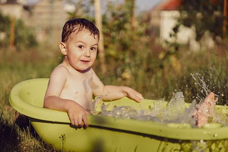 可爱的小男孩在花园里的户外浴缸里洗澡。