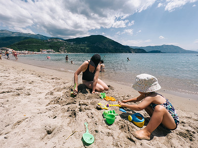 妈妈和小女孩坐在沙滩上雕刻沙雕