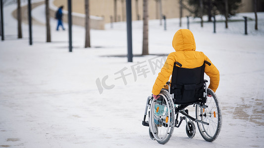 残障人士康复摄影照片_冬天，白人残疾妇女坐在公园的椅子上。