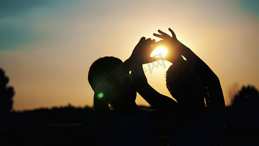 太阳夏天摄影照片_夏季日落时分，儿童、男孩和女孩的剪影、人物形象在太阳的背景下用手指、手展示心灵。