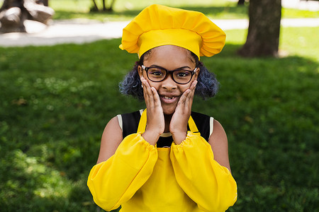 身穿厨师帽和黄色围裙制服的黑人非洲儿童厨师女孩震惊地双颊和惊喜。