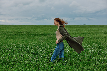 春天的田野摄影照片_多云多风的天气里，一位身穿外套的女士站在绿色田野里，双手插在口袋里